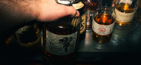 Mann nimmt eine Flasche Whiskey aus dem Schrank
