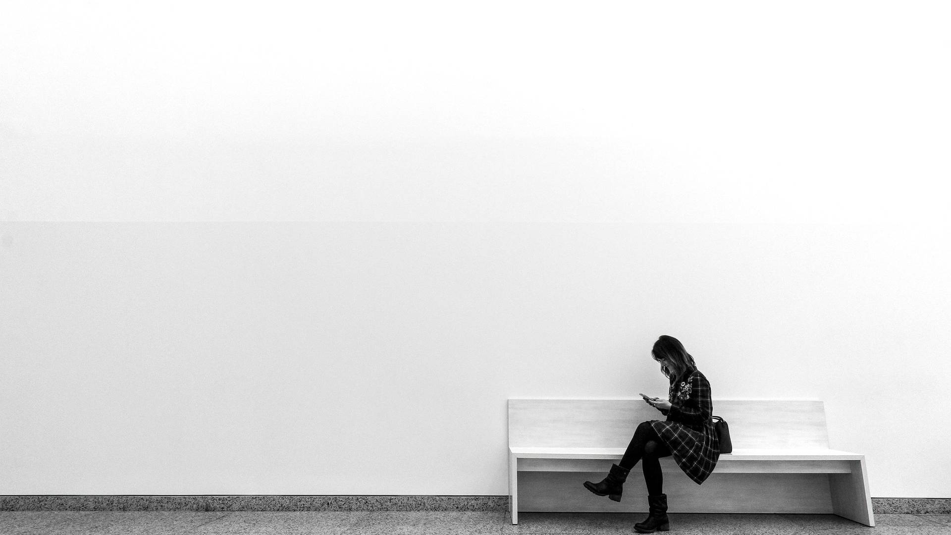 Frau sitzt auf einer Bank in einem leeren Raum und blickt auf ihr Handy